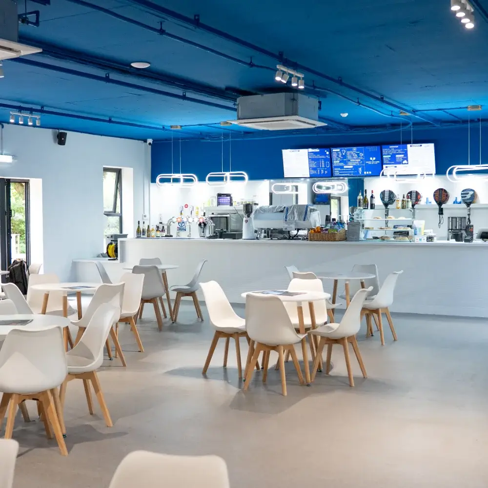 Court De Padel café seating area with white tables and counter service
