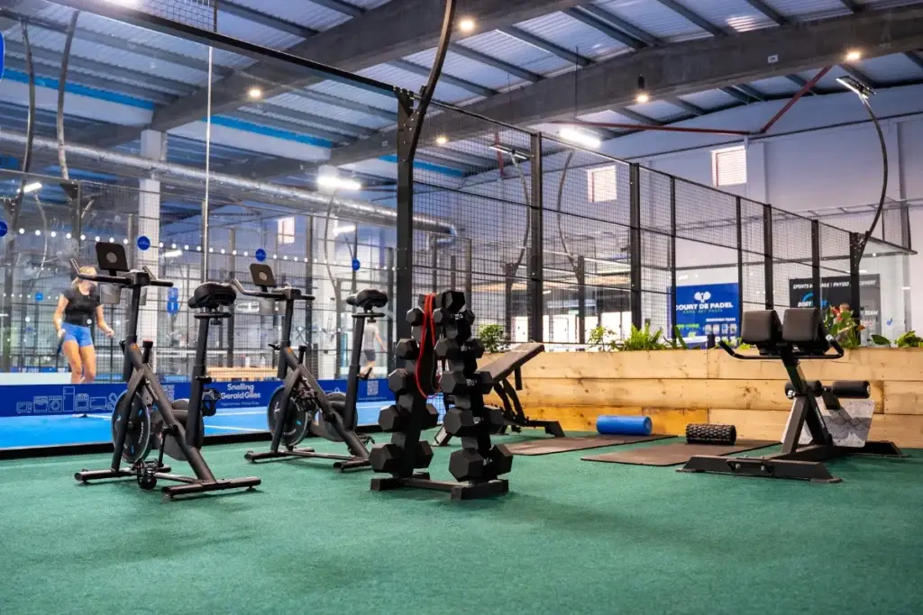 Indoor gym equipment area at Court De Padel overlooking the padel courts