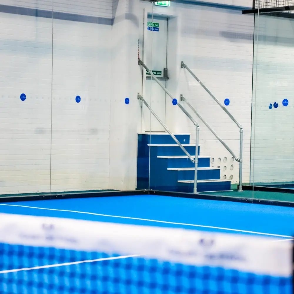 Indoor padel court at Court De Padel with glass walls and blue playing surface